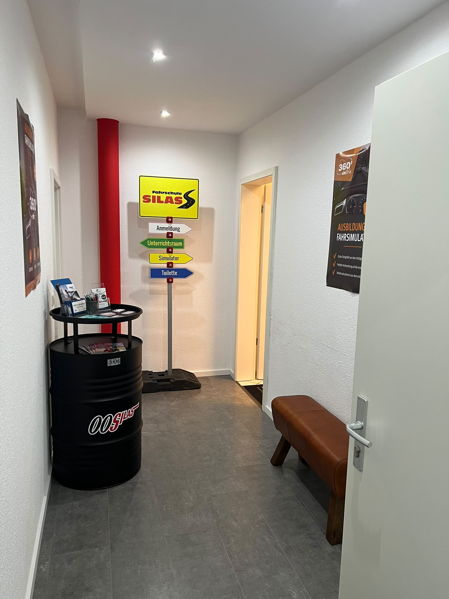 Flur in Waibstadt mit Wegweiser zu Anmeldung, Unterrichtsraum und Simulator, daneben ein 00Silas-Fass mit Flyern